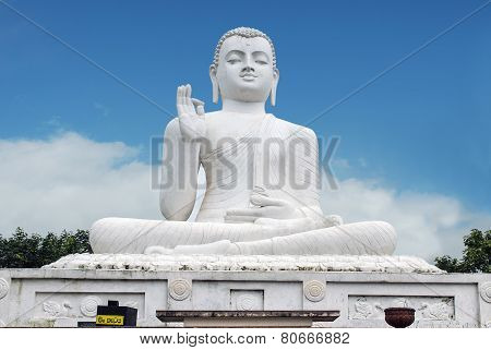 White statue of seated Buddha -Siddharta Gautama - with a raised right hand in a gesture of 