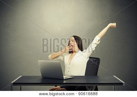 tired woman sitting with laptop and yawning over dark background
