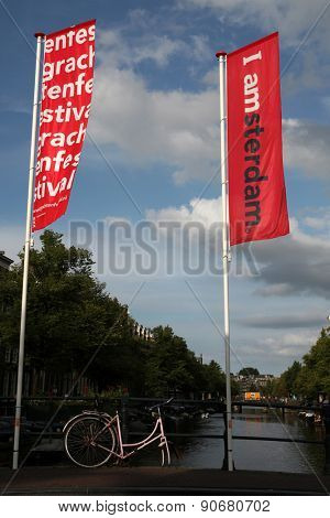 AMSTERDAM, NETHERLANDS - AUGUST 9, 2012: Old pink bicycle parked on the bridge decorated with banners with an official brand of the city in Amsterdam, Netherlands.
