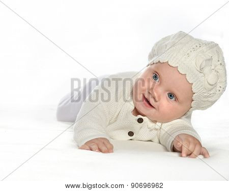 baby girl child lying down on white blanket smiling happy  fashion portrait face studio shot isolated on white caucasian  hat warm cloting