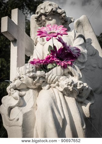 Mournful angel statue with flowers in cemetery