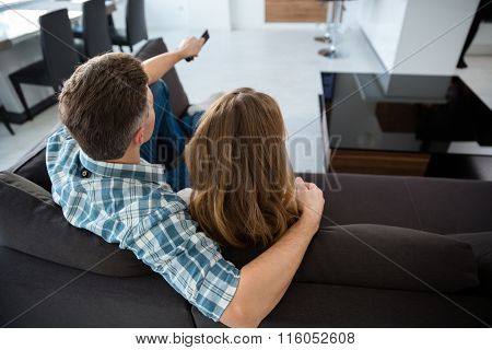 Back view of beautiful couple watching tv on sofa in living room 