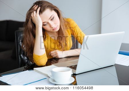 Sad woman sitting at the table with bills and laptop computer at home