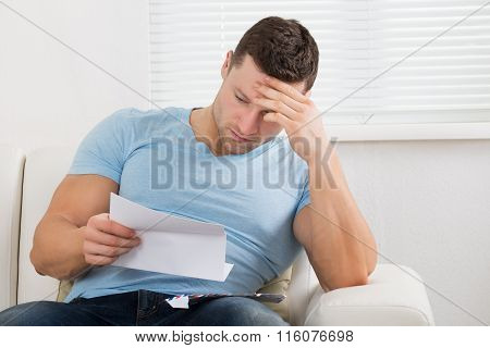 Upset Man Reading Letter On Sofa At Home