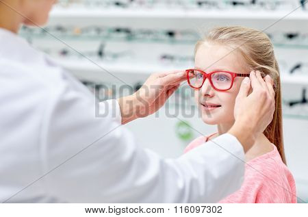 optician putting glasses to girl at optics store