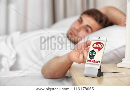 Beautiful young man waking up with mobile alarm clock