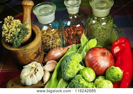 Glass bottles with spices, fresh vegetables, wooden mortar