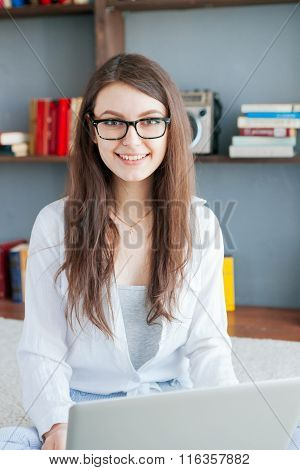 Happy young woman is relaxing on comfortable couch and using laptop at home.