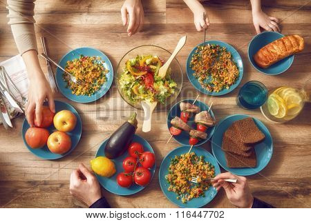 Top view of family having dinner together sitting at the rustic wooden table. Enjoying  family dinner together.
