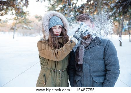 Amusing pretty young woman thowing snowball in her boyfriend face 