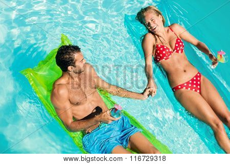 Peaceful couple on lilos holding cocktails in the pool