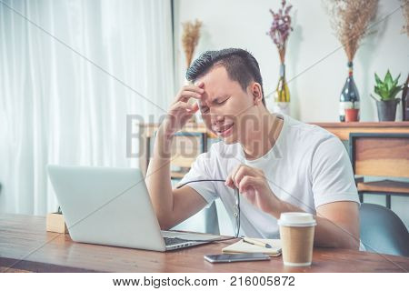 Sad Asian businessman crying behind notebook computer at cafe