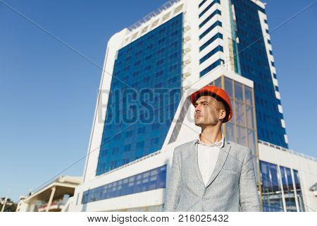 Unshaven Successful Business Man In Gray Suit And Protective Construction Orange Helmet On Building