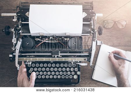 top view of man taking notes besides vintage manual typewriter on rustic wooden table