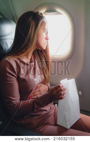 Girl is sick in the airplane and seating with paper pocket