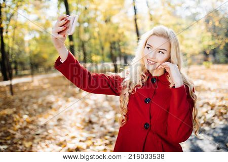Teenage Girl In Autumn In Park Taking A Selfie On Smart Phone. Beautiful Happy Young Woman Taking A