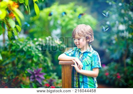 Little blond preschool kid boy discovering flowers, plants and butterflies at botanic garden. Schoolchild interested in biology. Active educational leisure with preschool kids in museum.
