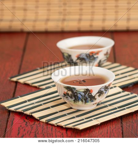 Vintage Chinese tea cup. Two white cups on bamboo mat for tea ceremony. Red rustic background