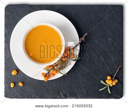 Tea of sea-buckthorn on a black slate stone. A branch of sea-buckthorn. White cup is a top view. Isolated on white background.