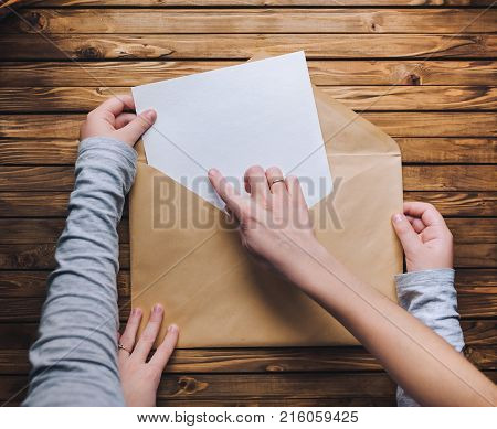 Mom and daughter open a large brown envelope and take out a letter or a clean white sheet of paper. Wooden background.