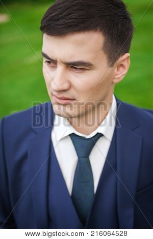 Portrait of handsome, thoughtfull asian groom in a dark blue against the backdrop of green meadow. concept of a strong successful man