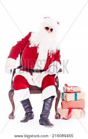 Portrait of swaggy Santa Claus in sunglasses relaxing in chair on white background