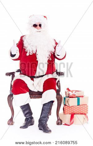 Portrait of swaggy Santa Claus in sunglasses relaxing in chair on white background