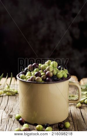 closeup of a handled enamelware pot full of arbequina olives from Catalonia, Spain, on a wooden rustic table, against a dark background with a blank space on top