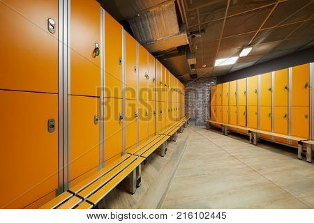 Locker room with rows of orange lockers at fitness center.