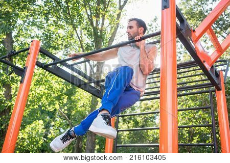 Low-angle view of a strong and determined young man doing amazing pull-up variation during extreme outdoor workout in the applauses of his friends