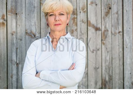 Portrait of a confident senior woman looking at camera while wearing a spotless shirt against a rustic wooden fence