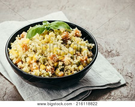 Close up view of cauliflower rice with vegetables. Organic paleo Cauliflower Rice with corn, green peas and carrots on brown concrete background. Copy space.