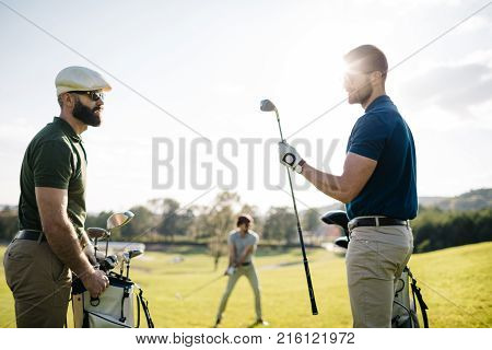 Stylish multicultural friends spending time together while playing golf on golf course