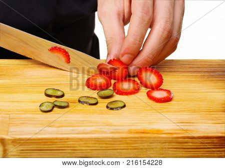 Close-up of the chef's chef's hands cut into a wooden board, where already there is grapes, a ripe strawberry
