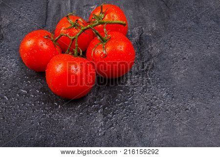 Ripe, juicy, appetizing, bright tomatoes on a green branch, lie on a black background.