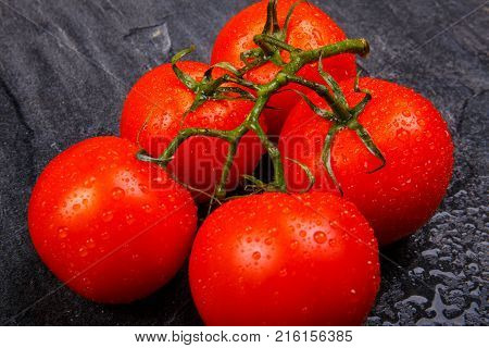 Ripe, juicy, appetizing, bright tomatoes on a green branch, lie on a black background.