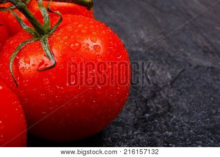 Close-up of mature, juicy, appetizing, bright tomatoes with water drops, on a green branch, lie on a black background.