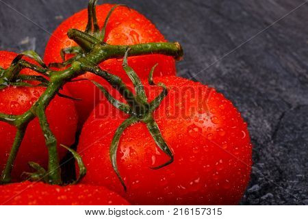 Close-up of mature, juicy, appetizing, bright tomatoes with water drops, on a green branch, lie on a black background.