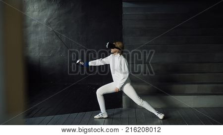 Concentrated young fencer woman practice fencing exercises using VR headset and training simulator competition game indoors