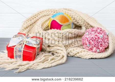 Christmas and new year balls and gift box in winter knitted scarf on wooden background
