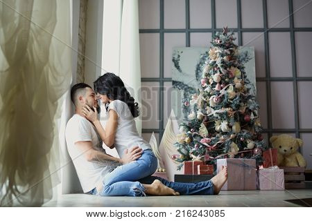 Beautiful young couple in love decorating Christmas tree, arranging the christmas lights and having fun