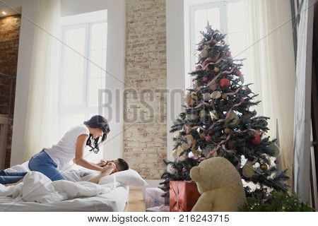 Beautiful young couple in love decorating Christmas tree, arranging the christmas lights and having fun