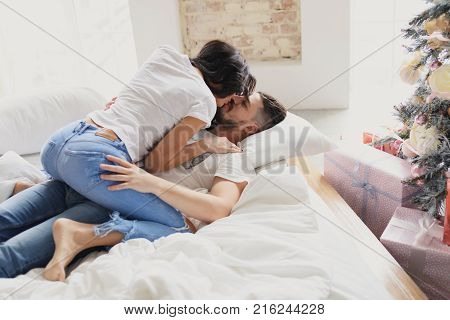 Beautiful young couple in love decorating Christmas tree, arranging the christmas lights and having fun