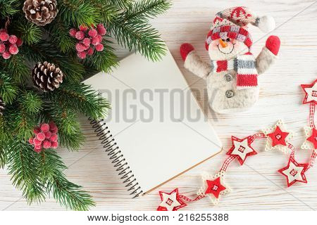 New Year background with Christmas tree, toy snowman and empty note greeting card on white wooden surface. Top view.