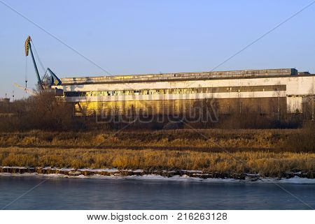 covered dock of ship repair yard for river ships on the overgrown with dry grass and bushes bank of the canal in the setting sun
