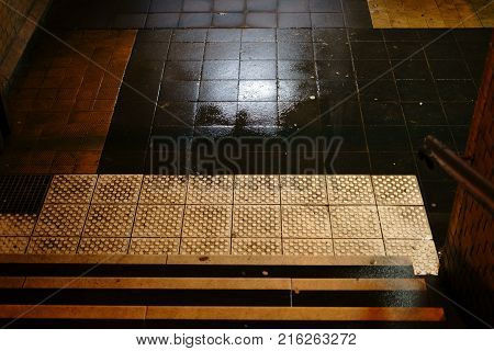 The dark steps of a station tunnel with puddles and damp walls.