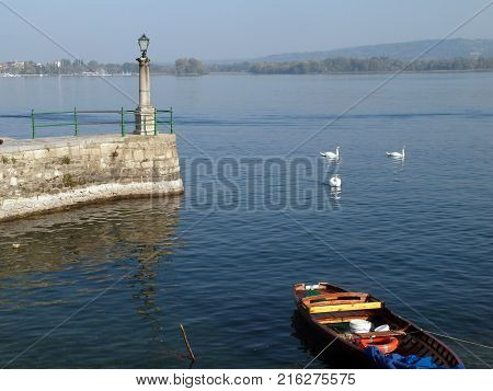 View of Lake Maggiore from the coast of Arona with streetlight pier boat and swans