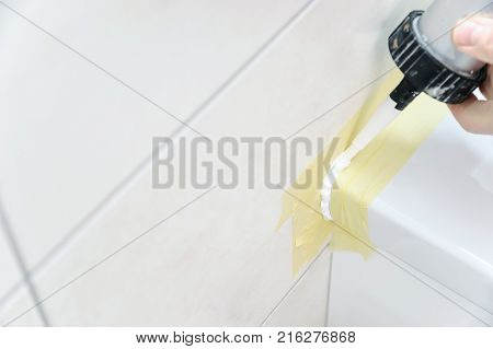 A man is puting the silicone sealant to caulk the joint between a washbasin and a wall.