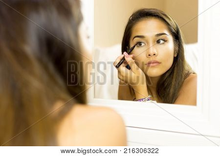 Reflective mixed race young woman with brush eye liner on with looking in the mirror