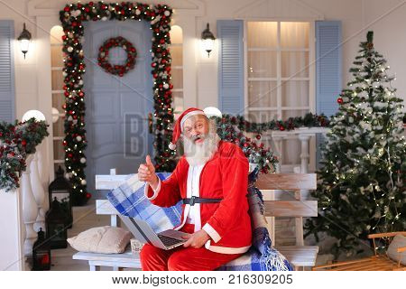 Cheerful Santa Claus making video call in cozy apartments. Gladden man in red costume satisfying with joyful ambience. Concept of communication with Father Christmas using modern gadget.